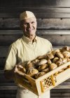 Happy baker carrying crate of bread rolls — Stock Photo