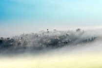Vista di villaggio nebbioso a montagne contro cielo azzurro — Foto stock