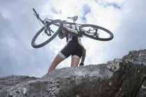 Joven llevando bicicleta de montaña en la cima de la roca - foto de stock