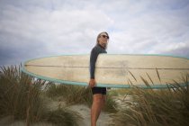 Портрет пожилой женщины на песке, держащей доску для серфинга — стоковое фото