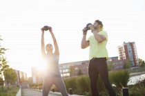 Woman and personal trainer holding up kettlebells at riverside — Stock Photo