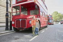 Two young brothers standing in front of red bus, London, UK — Stock Photo