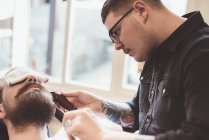 Barber using clippers on client beard in barber shop — Stock Photo