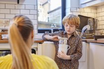 Boy carrying stack of mugs in kitchen — Stock Photo