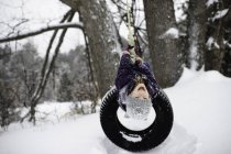 Girl upside down on tire swing in snow — Stock Photo