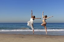 Dos jóvenes bailarinas saltando en el aire en la playa - foto de stock
