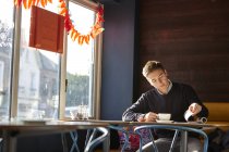 Young man alone in cafe drinking coffee and reading magazine — Stock Photo