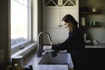 Donna che riempie tazza al lavello della cucina — Foto stock