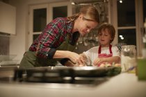 Зрелая женщина помогает сыну с выпечкой на кухне — стоковое фото