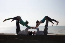 Silhouetted men and women practicing acrobatic yoga on wall at Brighton beach — Stock Photo