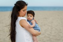 Мати на пляжі носить дитину в руках — стокове фото