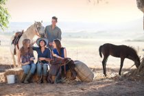 Cuatro jóvenes amigos sentados en la paca de heno con caballos - foto de stock