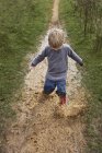Мальчик-дошкольник, плескающийся в грязной луже в сельской местности — стоковое фото