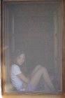 Retrato de menina sentada na moldura da janela obscurecida — Fotografia de Stock