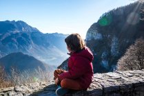 Boy sitting on wall looking out at mountain landscape, Italy — Stock Photo