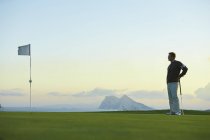 Golfista segurando clube de golfe em pé perto da bandeira de golfe olhando para longe — Fotografia de Stock