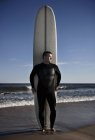 Портрет взрослого мужчины, стоящего с высокой доской для серфинга на пляже — стоковое фото