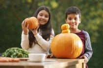 Portrait of brother and sister in garden holding pumpkins — Stock Photo