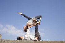 Uomo e donna sul muro che praticano lo yoga acrobatico — Foto stock