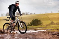 Homme à vélo de montagne à travers la boue — Photo de stock