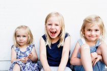 Portrait of three young sisters sitting in front of white wall — Stock Photo