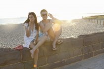 Young couple sitting on wall, woman eating ice cream, Port Melbourne, Melbourne, Australia — Stock Photo