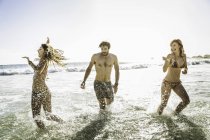 Três amigos adultos vestindo biquínis e shorts de natação salpicando no mar, Cape Town, África do Sul — Fotografia de Stock