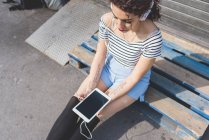 Жінка сидить на піддоні в навушниках, що тримають цифровий планшет — стокове фото