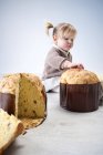 Female toddler sitting on floor with fingers on pannetone cake — Stock Photo