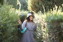 Mature woman wearing sunhat and cardigan touching plants, looking away smiling, Seville, Spain — Stock Photo