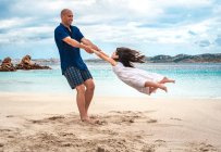 Homme adulte balançant sa fille sur la plage, La Maddalena, Sardaigne, Italie — Photo de stock