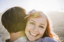 View over shoulder of woman hugging man, looking at camera smiling — Stock Photo