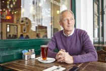Mature man looking out from sidewalk cafe table — Stock Photo