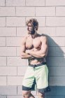 Jeune entraîneur masculin à poitrine nue appuyé contre un mur à l'extérieur de la salle de gym — Photo de stock