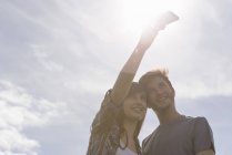 Молодая пара делает селфи на мобильном телефоне под ярким солнечным небом — стоковое фото