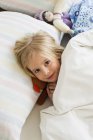 Портрет маленькой блондинки, лежащей в постели с куклой — стоковое фото