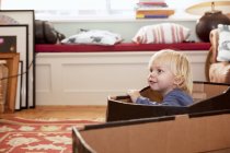 Мальчик играет в картонной коробке в гостиной — стоковое фото