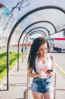 Young woman with dreadlocks using smartphone touchscreen in urban bus shelter — Stock Photo
