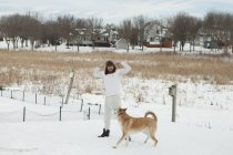 Молодой человек в нижнем белье и меховой шапке играет с собакой в снегу — стоковое фото