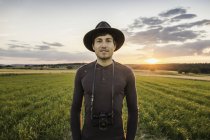 Портрет человека, стоящего в поле с камерой SLR вокруг шеи — стоковое фото