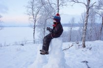 Мальчик сидит на вершине снеговика, Хемаван, Швеция — стоковое фото