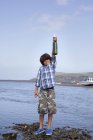 Niño sosteniendo mensaje en botella en la playa - foto de stock