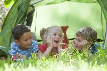 Trois enfants couchés bavardant dans une tente de jardin — Photo de stock