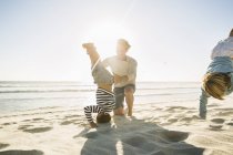 Father on beach helping son doing handstand — Stock Photo