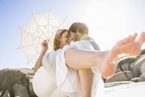 Man carrying woman holding lace umbrella in arms face to face smiling — Stock Photo