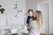 Mitte erwachsene Frau küsst Baby-Sohn im Wohnzimmer auf die Wange — Stockfoto