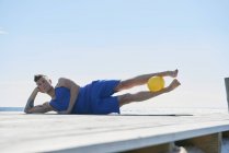 Mann auf Pier liegend auf Ellbogen gestützt, Ball zwischen den Beinen — Stockfoto