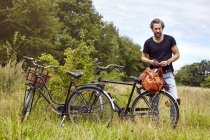 Male cyclist unpacking holdall  in rural field — Stock Photo