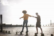 Мужчина помогает женщине балансировать на деревянных пнях на пляже — стоковое фото