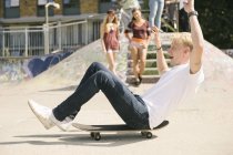 Young male skateboarder sitting on skateboard on the move in city skatepark — Stock Photo